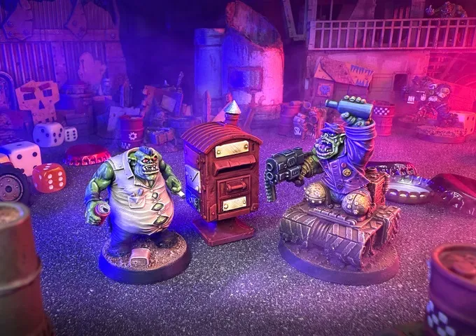 Two colorful miniatures of space orcs are prominently featured in a chaotic urban setting. On the left, a green orc in a tattered shirt stands next to a mailbox, while on the right, another orc raises a weapon triumphantly, showcasing a muscular build and a blue outfit. The background is filled with various scattered objects, including dice and barrels, illuminated by a mix of purple and blue lighting, enhancing the vibrant and chaotic atmosphere of the scene.