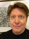 A close-up portrait of a man with light brown hair and striking green eyes, smiling slightly. He is wearing a black shirt and is positioned in front of a detailed, artistic background featuring a complex, fantastical structure, possibly a building or landscape. The overall tone of the image is casual and inviting, with a focus on the subject's expressive features.