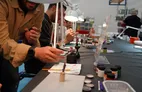People painting miniatures at a table with lamps and art supplies.