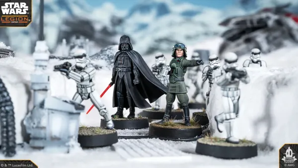 A detailed scene features Darth Vader standing prominently with his red lightsaber drawn, dressed in his iconic black armor and cape. Flanking him are two Stormtroopers, one aiming a blaster, set against a snowy landscape with scattered debris and structures. The miniatures are mounted on circular bases, showcasing their intricate designs and the dynamic pose of the characters.