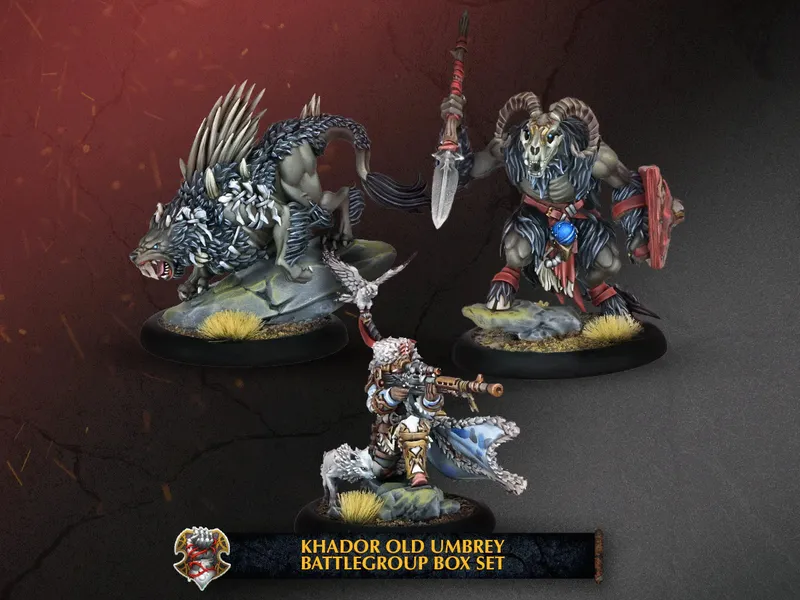 A trio of miniatures from the Khador Old Umbrey Battlegroup Box Set is displayed against a dark, textured background. On the left, a fierce, wolf-like warbeast with spiky fur stands on a rocky base, while in the center, a character wielding a rifle is dressed in fur-lined clothing, poised for action. To the right, a heavily muscled figure with a ram-like head brandishes a spear and shield, adorned with tribal elements. The bottom of the image features a banner with the text "KHADOR OLD UMBREY BATTLEGROUP BOX SET."