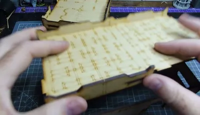 Hands holding a wooden MDF building piece with etched details.