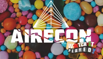 A colorful assortment of candies in various shapes and sizes serves as the backdrop for the event branding. The word "RECON" is prominently displayed in bold white letters, with a stylized triangular logo above it. Below, the text "with WATCH PLAYED" is featured in a playful font, suggesting a fun and engaging gaming event.