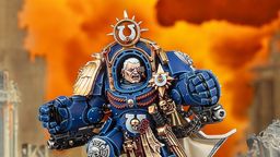 A detailed miniature of Marneus Calgar, a prominent character from the Warhammer 40,000 universe, is depicted in a striking pose. He wears ornate blue power armor adorned with gold embellishments, featuring a prominent Ultramarines symbol on his chest and a skull motif. The background is a dramatic orange, suggesting a fiery battlefield, enhancing the intensity of the scene.