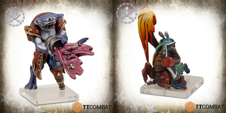 Two colorful miniatures are displayed side by side on clear bases. On the left, a vibrant purple creature with a rounded body and various textures, featuring small eyes and a playful expression. On the right, a detailed figure resembling a crab or lobster, adorned with a flowing orange and yellow flame-like appendage, wearing a blue and green outfit, and showcasing intricate detailing on its claws and body.
