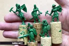 A hand holding several green resin miniatures from the "Ladies Only" collection by Scibor Monstrous Miniatures. The miniatures depict various fantasy female characters, including a warrior with an axe and shield, a knight, and a pirate, all standing on cork bases. The text "Ladies set 2" is displayed at the bottom of the image.