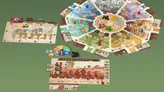 A colorful board game layout with maps, tokens, cards, and player pieces on a green background.