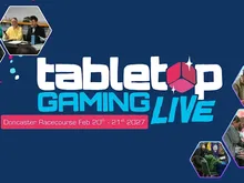 Bright blue background with white, pink, and cyan text reading "tabletop GAMING LIVE" and "Doncaster Racecourse Feb 20th - 21st 2027." Two inset photos show people seated at tables with gaming pieces.