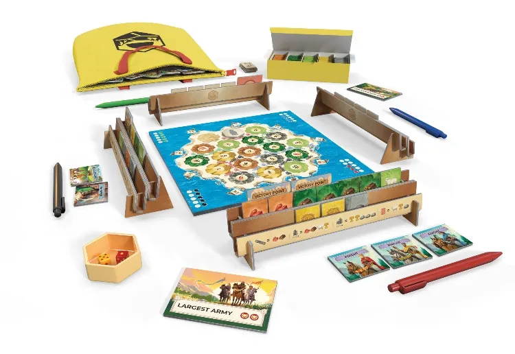 A portable version of Catan, titled Catan Zip!, is displayed with various components spread out. The central focus is a colorful game board featuring hexagonal tiles representing different resources, surrounded by punchboard tile holders and resource tokens. Additional items include a yellow travel bag, themed pens, a dice shaker, and cards for development and achievements, all arranged neatly for easy access during gameplay.