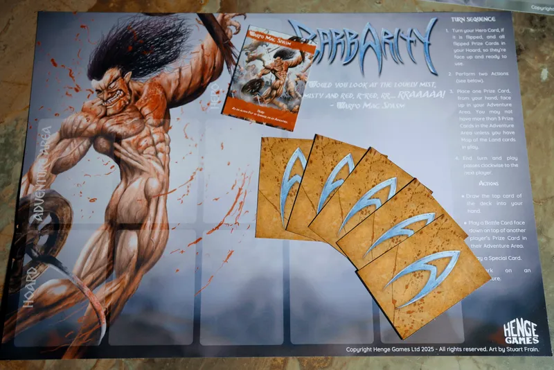 The image features a game board for the card game "Barbarity," prominently displaying a muscular barbarian character with long, wild hair and a fierce expression, depicted in a dynamic pose. The background is splattered with red, suggesting a violent theme. To the right, there are several game cards, including one labeled "Warpo Mac Spasm," alongside a set of prize cards that have a textured, brown appearance with stylized blue markings. The board has designated areas for adventure cards, emphasizing the game's focus on combat and resource management.