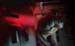 A large, monstrous figure with glowing red eyes and exposed teeth crouches in a dimly lit, abandoned hallway. The creature wears a tattered red shirt and greenish pants. A red illuminated "EXIT" sign is visible on the left wall.