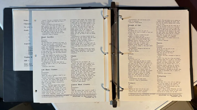 A three-ring binder containing the playtest manuscript for "ManaStorm: The Magic Adventure Game," featuring several pages of text. The visible pages include sections titled "Blood Sacrifice," "Call Black Creature," and "Chains," detailing game mechanics and spell effects. The binder also holds character sheets and player handouts, with a focus on the game's core mechanics and aspects related to the Colors of Magic.
