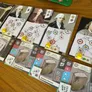 Board game cards featuring portraits of three historical figures, each with colored circular diagrams and numbered slots. Below, labeled cards show specimens: "Micographia" with a magnified insect, "Systema Naturae" with a rock and butterfly. Arabic and English text visible. Wooden table surface.
