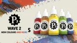 Four bottles of P3 paint are displayed against a colorful, textured background. The bottles include "Gunner Red," "Menite Ochre," "Radiant Yellow," and "Witchfire Green," each featuring a black gear logo with "P3" prominently displayed. The background features splashes of blue, red, and white paint, adding a vibrant artistic flair to the scene.