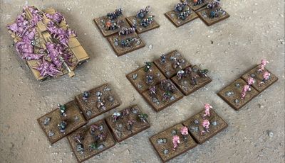 A collection of Zayken miniatures from Void Scar Miniatures is displayed on a textured surface. In the foreground, several bases feature hordes of zombified figures in various colors, including green, purple, and pink, representing the Neophyte Mobs. To the left, a tank is adorned with grotesque, bloated creatures, suggesting a fusion of machine and undead, while additional bases of zombies are scattered throughout the scene, emphasizing the overwhelming numbers of the Zayken forces.