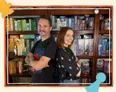 Felicia Day and Wil Wheaton standing with arms crossed in front of a bookshelf filled with board games.
