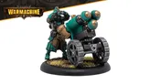 A Crucible Guard Mechanik stands beside a large, wheeled artillery piece, showcasing a blend of teal and brown armor with intricate detailing. The Mechanik is equipped with goggles and a tool belt, emphasizing their role in maintaining war machines. The base features tufts of grass, adding a touch of realism to the miniature's presentation.