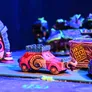 A colorful miniature vehicle designed for a racing game, featuring a pink body with a whimsical spiral design and a castle-like turret on top. In the background, other fantastical vehicles and structures are visible, set against a vibrant, illuminated tabletop environment. The scene captures a playful and chaotic atmosphere, fitting for a greenskin-themed racing skirmish.