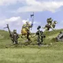 A group of halfling miniatures stands on a grassy terrain, showcasing their unique characteristics. In the center, a halfling in ornate armor rides a large, lion-like creature, holding a blue and white banner. To the left, another halfling wields a spear, while a third, dressed in green, brandishes a hammer. A fourth halfling rides a smaller, dog-like creature, completing the ensemble of pint-sized warriors. The background features a soft blue sky with scattered clouds, enhancing the whimsical atmosphere.