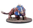 A detailed miniature of a Plague Colossus, a large, monstrous creature, is depicted on a textured base. The creature features a rugged, reddish-brown body with blue armor-like plates and prominent spikes, showcasing a fierce expression with sharp teeth and glowing eyes. Its muscular limbs and claws emphasize its intimidating presence, making it a striking addition to any sci-fi wargaming setup.