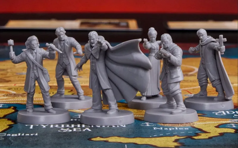 Five detailed gray miniatures are arranged on a colorful game board depicting a map of Europe. The central figure, Dracula, is depicted with a dramatic pose, wearing a flowing cape and extending one arm forward. Surrounding him are four hunters: one holds a stake, another appears to be aiming a weapon, while the others are dressed in Victorian attire, ready for the hunt. The game board features various geographical labels, including the "Tyrrhenian Sea," enhancing the thematic setting of the game.
