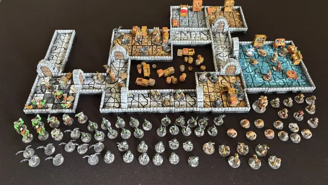A detailed 15mm scale dungeon setup features modular tiles arranged to create a labyrinthine environment, complete with stone walls and various furniture pieces like crates and barrels. Scattered throughout the dungeon are numerous painted miniatures representing a brave group of heroes and a variety of monsters, including orcs and giant spiders. The scene is set against a dark background, enhancing the vibrant colors of the miniatures and the intricate details of the dungeon tiles.