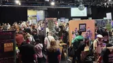 Crowd at a gaming convention with booths, a "Square Devil" sign, and a screen reading "FLIP Flippers!"