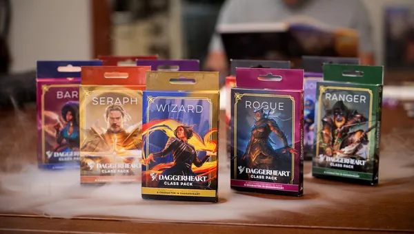 Four colorful Class Packs for the Daggerheart tabletop roleplaying game are displayed prominently. The packs are labeled "BARBARIAN," "SERAPH," and "WIZARD," each featuring unique artwork representing the respective classes. The background includes a soft, smoky effect, enhancing the fantasy theme of the scene.