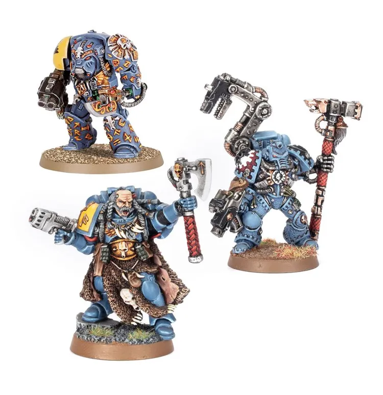 Three Space Wolves miniatures are displayed, showcasing their distinctive blue armor and intricate details. On the left, a Space Marine in a power armor suit features a large shoulder pad and a bolter. In the center, a character with a fur-lined cloak wields a power axe, while on the right, another Space Marine holds a hammer and has a mechanical arm. Each figure stands on a textured base, highlighting their unique poses and weaponry.