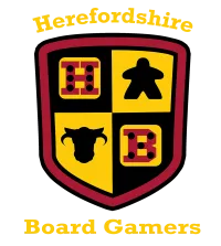 A shield-shaped logo features a divided design with four quadrants. The top left quadrant displays a red die with black dots, the top right features a black meeple, the bottom left shows a black cow silhouette, and the bottom right has a red die with white dots. The text "Herefordshire Board Gamers" is prominently displayed above and below the shield in a bold, yellow font.