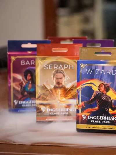 Four colorful Class Packs for the Daggerheart tabletop roleplaying game are displayed prominently. The packs are labeled "BARBARIAN," "SERAPH," and "WIZARD," each featuring unique artwork representing the respective classes. The background includes a soft, smoky effect, enhancing the fantasy theme of the scene.
