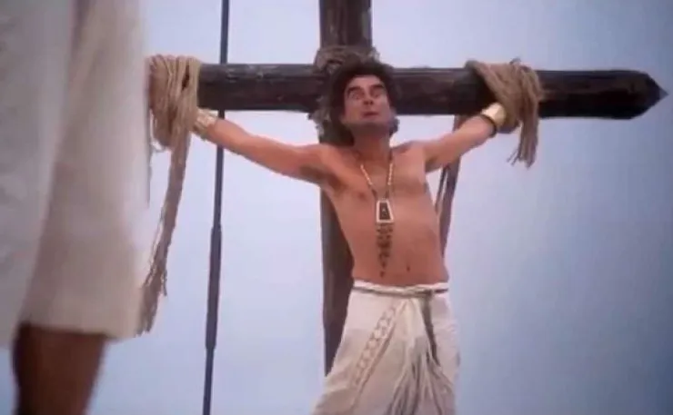 Movie still of crucifixion theme from 'The Life of Brian' where a man is bound to a cross.