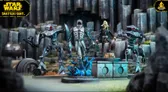 A detailed scene showcases several miniatures from the Star Wars: Shatterpoint game. In the foreground, a Quarren character stands on a base with blue, swirling water effects, while a humanoid figure in a gray suit, holding a weapon, is positioned nearby. To the left, a droid with a sleek design and red accents is poised, and in the background, a second droid stands ready for action against a backdrop of rocky terrain and structures, enhancing the dynamic atmosphere of the scene.