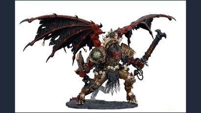 A large, intricately detailed statue of Angron, the Daemon Primarch of Khorne, stands prominently. He features massive, bat-like wings and a fierce expression, with a head that appears relatively small compared to his muscular body. Adorned with skulls and ornate armor, he wields a large sword in one hand and a weapon in the other, standing on a textured base that enhances the dramatic effect of the figure. The color palette includes deep reds, blacks, and metallic tones, emphasizing his menacing presence.