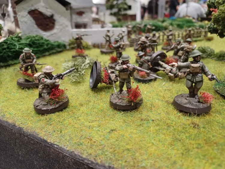 A detailed diorama showcases a World War I battlefield scene, featuring miniature soldiers from the US Marine Corps and German army. The figures are positioned on a grassy terrain, with some soldiers holding rifles and others engaged in various actions, surrounded by patches of red foliage. In the background, there are model buildings and trees, enhancing the immersive atmosphere of the display.