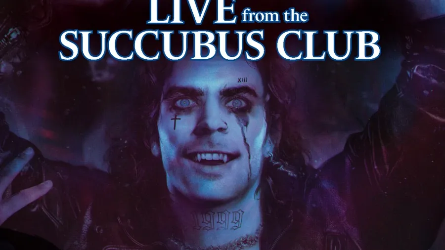 A vampire with pale skin and striking blue eyes is depicted in a dark, atmospheric setting, wearing a leather jacket and showcasing numerous tattoos across his chest and neck. His expression is exuberant, with a wide smile and streaks of dark makeup running down his face, suggesting a rock star persona. The background features a blend of purple and blue hues, enhancing the club-like ambiance, while the title "LIVE from the SUCCUBUS CLUB" is prominently displayed at the top.