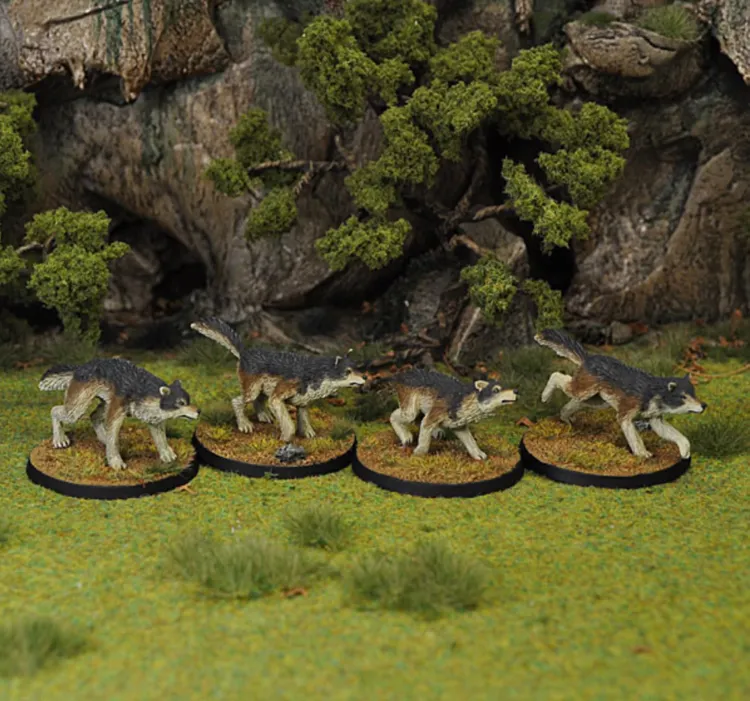 Four fantasy wolf miniatures are displayed on a grassy terrain, each mounted on a circular base. The wolves have detailed fur textures, featuring dark gray and brown coloring, with some showing dynamic poses as if in motion. In the background, there are small trees and rocky formations, enhancing the natural setting.