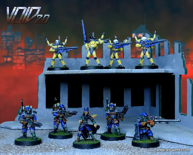 A group of miniature figures is displayed on a ruined building set against a dramatic, fiery background. The upper level features four yellow-armored soldiers, each holding blue weapons, while the lower level showcases three figures in blue attire, one with a cloak, all armed and posed in various stances. The scene captures a dynamic confrontation, emphasizing the contrasting colors of the figures against the gray structure and vibrant backdrop.