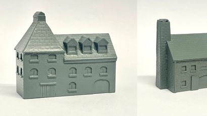 A detailed model of a building designed for 6mm scale wargames, featuring a sloped roof with three dormer windows and a textured surface that resembles slate. The facade includes several arched and rectangular windows, along with a large door at the base, all rendered in a light gray resin. The overall design suggests an industrial style, suitable for various historical or modern warfare settings.