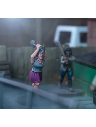 A dynamic scene features three miniature figures in a tense urban setting. In the foreground, a woman with blue hair raises a shovel, while a second figure behind her holds a baseball bat, both appearing ready to confront a threat. A third figure, dressed in a light shirt and blue pants, is seen running away, adding to the sense of urgency in the scene, with a green dumpster and a wooden fence in the background.