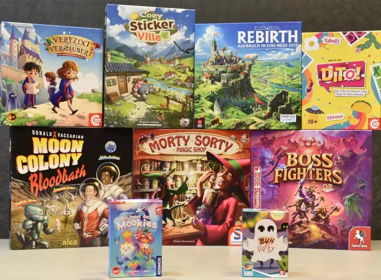 A collection of board game boxes is displayed, showcasing the nominees for the Spiel des Jahres awards. The top row features "Verflixt Verzaubert," "Cozy Sticker Ville," "Rebirth," and "Dittto!" with colorful artwork depicting whimsical scenes and characters. The bottom row includes "Moon Colony Bloodbath," "Morty Sorty Magic Shop," "Boss Fighters QR," and "Die Insel der Mookies," along with "Buh Party," all featuring vibrant illustrations that highlight their themes and gameplay.
