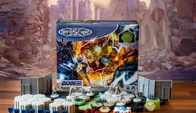 A G.I. JOE Heroscape: Rumble at the Rift Battle Box is prominently displayed in the center, featuring vibrant artwork of characters in action. Surrounding the box are various game components, including eight miniatures representing characters like Duke and COBRA Commander, modular hex terrain pieces, COBRA fortifications, dice, and markers. The background features a blurred, crumbling environment, enhancing the game's adventurous theme.