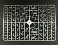 A plastic sprue featuring various components for miniature figures, including multiple torsos, limbs, and heads designed for 28mm scale modern civilians and post-apocalyptic survivors. The figures are in a gray plastic, arranged in a grid pattern, showcasing a variety of poses and accessories. The central part of the sprue includes a circular connector, with the pieces surrounding it neatly organized for easy access during assembly.