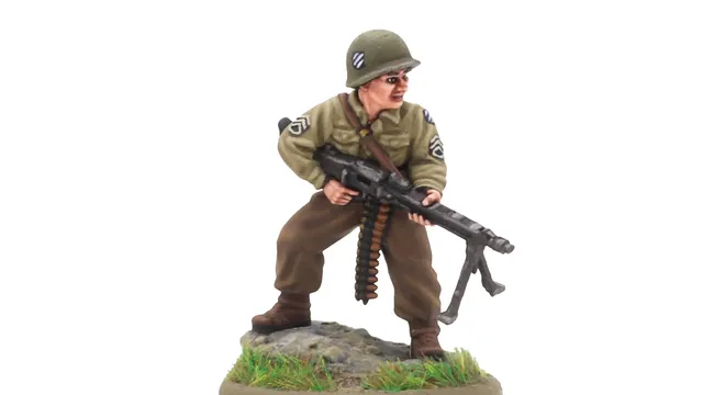 A 28mm scale miniature of a soldier, representing the war hero Audie Murphy, stands on a rocky base adorned with green grass. The figure is dressed in a light green military uniform with insignia on the sleeves and wears a helmet. He holds a machine gun in a ready position, showcasing a determined expression.