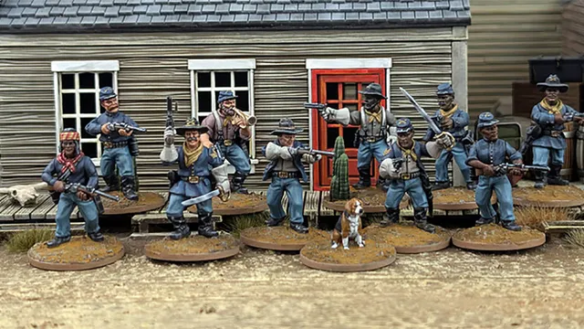 A group of ten detailed 28mm scale miniatures representing dismounted US Cavalry and Buffalo Soldiers stands in front of a wooden building with a red door. The miniatures are posed with various weapons, including rifles and a bugle, showcasing a mix of uniforms and accessories, such as scarves and hats. A small beagle and a cactus are also present among the figures, all mounted on 25mm round bases with a sandy terrain effect.