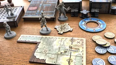 Two pirate miniatures are prominently displayed on a wooden table: one is a skeletal figure with a sword, and the other is a pirate with a tricorn hat and a hook for a hand. Nearby, a compass rose and a game board section titled 