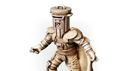 A gold-colored miniature figurine of a character wearing a cylindrical helmet resembling a trash bin, with a cape flowing behind. The figure stands on a round black base with a textured surface. The helmet has a handle on top and a small emblem on the front. The figure is posed with one arm extended forward and one leg slightly bent, as if mid-step.