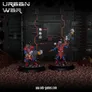 Two miniatures in futuristic combat gear stand on rocky terrain. One wears red and blue armor with a helmet and holds a large gun. The other has green and red armor with a helmet and a similar weapon. A dark, industrial background with glowing panels and text "URBAN WAR" appears above them.