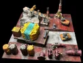 A detailed modular sci-fi terrain setup features various structures and elements, including a large yellow and blue container, a crane, and several industrial tanks in shades of gray and yellow. The terrain is painted with a mix of red and gray tones, creating a weathered, industrial look. Additional components like pipes and small vehicles are scattered throughout, enhancing the scene's complexity and depth for tabletop gaming.