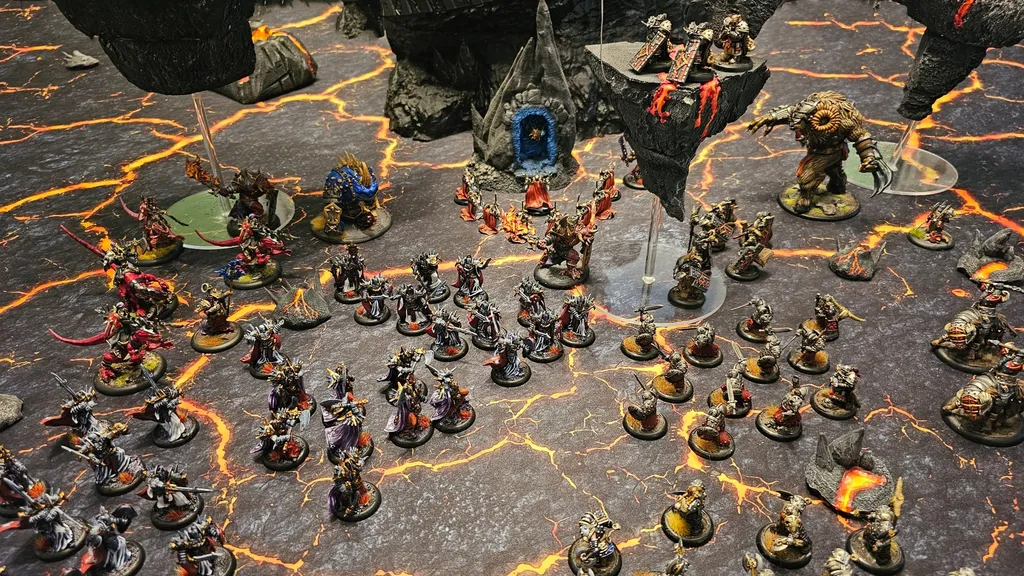 Miniature dark fantasy wargame scene with two armies on a cracked, lava-like battlefield. Left side features dwarven figures with armor and weapons, including a large blue-robed figure with a glowing orb.